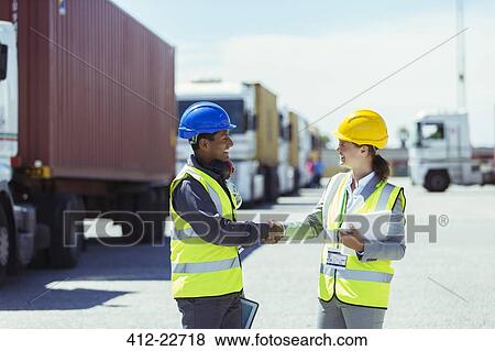 Stock Photo - Worker and businesswoman shaking hands near trucks and cargo containers. Fotosearch