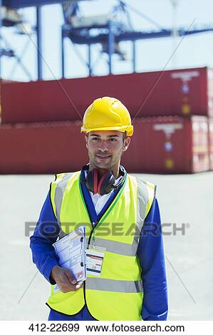 Stock Photo - Worker carrying clipboard near cargo containers. Fotosearch