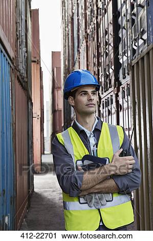 Stock Image - Worker standing between cargo containers. Fotosearch