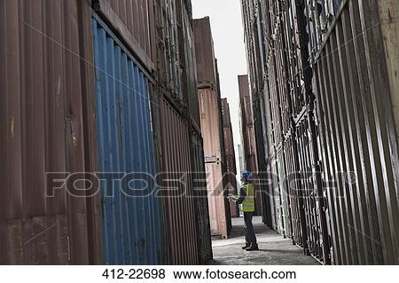 Worker standing between cargo containers View Large Photo Image Stock Photo - Worker standing between cargo containers. Fotosearch