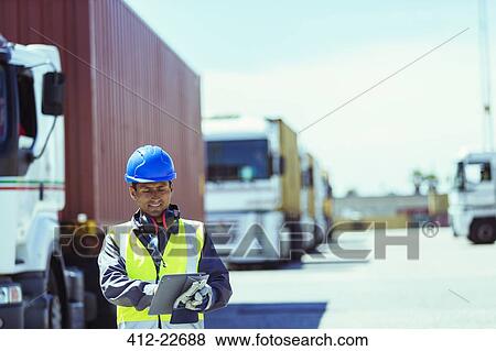 Stock Photo - Worker using digital tablet near trucks with cargo containers. Fotosearch
