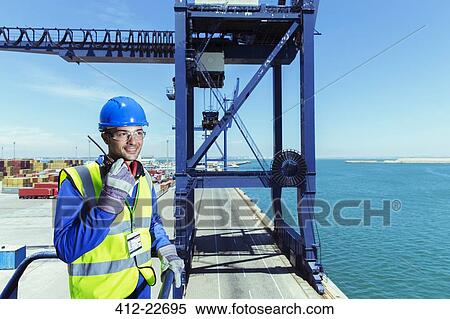 Stock Photography - Worker using walkie-talkie on cargo crane at waterfront. Fotosearch