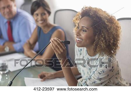 Beautiful woman sitting at conference table talking into microphone View Large Photo Image Stock Photo - Beautiful woman sitting at conference table talking into microphone. Fotosearch