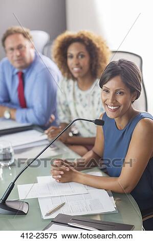 Beautiful woman sitting at conference table talking into microphone View Large Photo Image Stock Photography - Beautiful woman sitting at conference table talking into microphone. Fotosearch