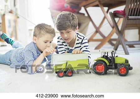 Stock Image - Brothers playing with toy tractor on floor. Fotosearch