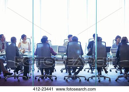 Stock Image - Business people having meeting in conference room, sitting with laptops and discussing. Fotosearch