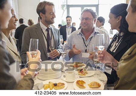Stock Photography - Business people standing by table in office, talking and drinking champagne. Fotosearch
