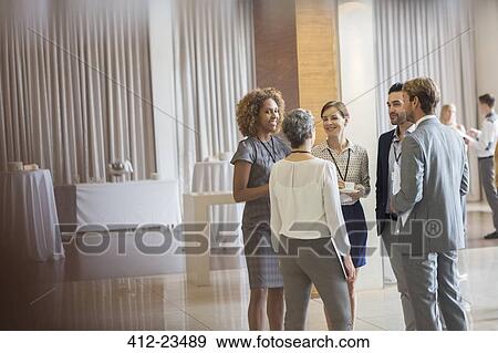 Stock Photo - Business people standing in conference room, talking and smiling. Fotosearch