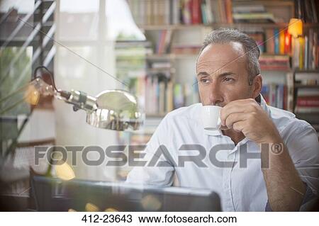 Stock Image - Businessman drinking cup of espresso in home office. Fotosearch
