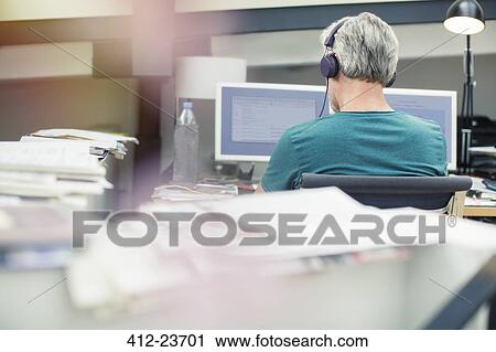 Stock Image - Businessman listening to headphones in office. Fotosearch