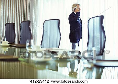 Businessman looking out of window and using mobile phone in conference room View Large Photo Image Stock Image - Businessman looking out of window and using mobile phone in conference room. Fotosearch