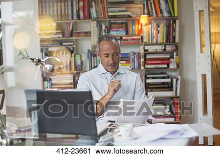 Businessman reading paperwork at home office desk View Large Photo Image Stock Image - Businessman reading paperwork at home office desk. Fotosearch