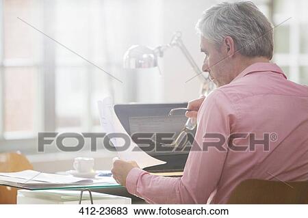 Businessman reading paperwork at home office desk View Large Photo Image Stock Image - Businessman reading paperwork at home office desk. Fotosearch