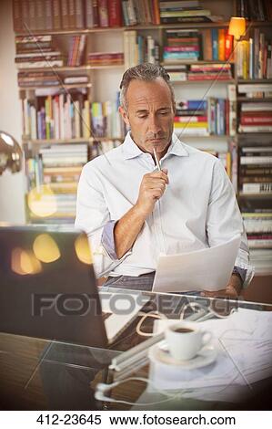 Stock Photography - Businessman reading paperwork at home office desk. Fotosearch