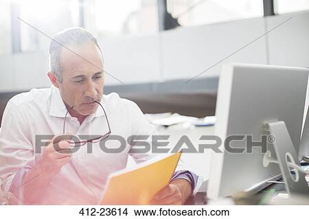 Businessman reading paperwork at office desk View Large Photo Image Picture - Businessman reading paperwork at office desk. Fotosearch