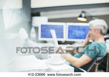 Stock Photograph - Businessman reading paperwork in office behind coffee cup. Fotosearch