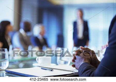 Stock Photography - Businessman sitting at conference table in conference room with hands clasped. Fotosearch