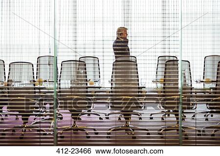 Businessman standing and using mobile phone in conference room View Large Photo Image Stock Photograph - Businessman standing and using mobile phone in conference room. Fotosearch