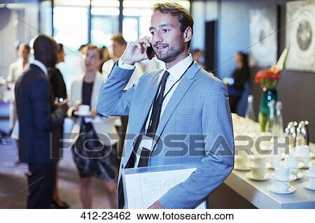 Stock Image - Businessman standing in office, holding document and using mobile phone. Fotosearch
