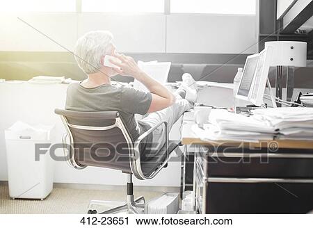 Stock Image - Businessman talking on cell phone at office desk. Fotosearch