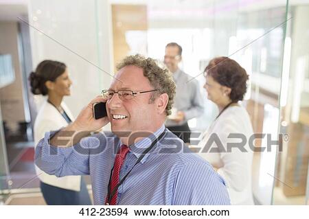 Businessman talking on mobile phone, colleagues standing in background View Large Photo Image Picture - Businessman talking on mobile phone, colleagues standing in background. Fotosearch