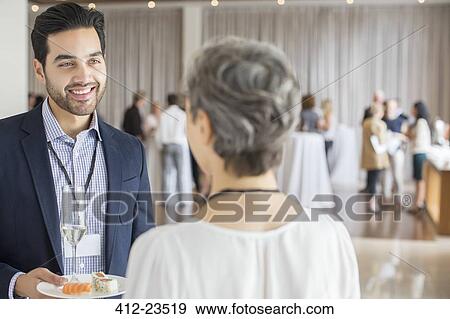 Businessman talking to businesswoman during reception in conference room, holding plate and champagne flute View Large Photo Image Stock Photo - Businessman talking to businesswoman during reception in conference room, holding plate and champagne flute. Fotosearch