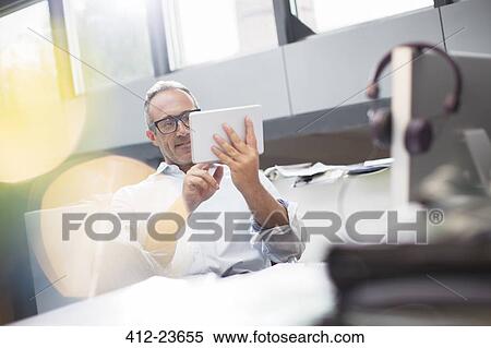 Stock Photography - Businessman using digital tablet at office desk. Fotosearch