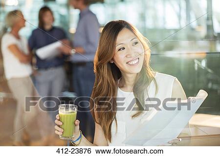 Businesswoman drinking juice and reading paperwork in office View Large Photo Image Stock Photograph - Businesswoman drinking juice and reading paperwork in office. Fotosearch