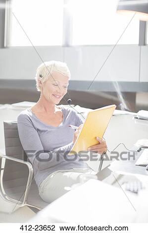Stock Image - Businesswoman in headset writing in notebook at office desk. Fotosearch