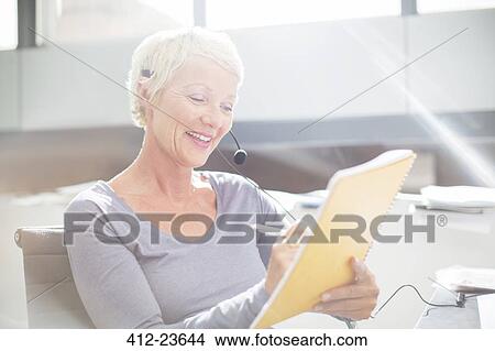 Picture - Businesswoman in headset writing on notepad in office. Fotosearch