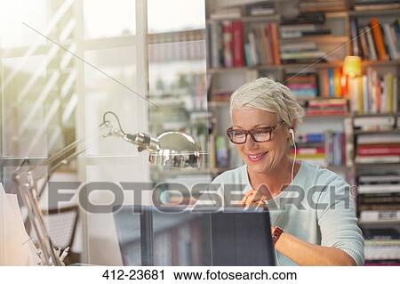 Stock Image - Businesswoman listening to earbuds and working in home office. Fotosearch