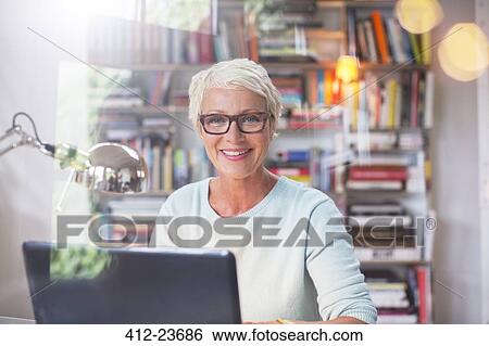 Businesswoman smiling at computer in home office View Large Photo Image Stock Photograph - Businesswoman smiling at computer in home office. Fotosearch