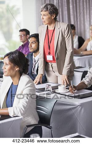 Stock Photograph - Businesswoman standing and asking question during presentation in conference room. Fotosearch