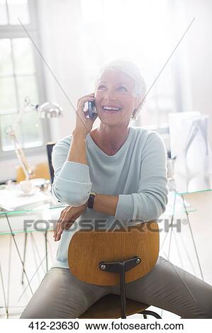 Stock Image - Businesswoman talking on cell phone in office. Fotosearch