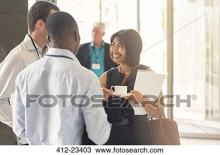 Stock Image - Businesswoman talking to colleagues holding coffee cup in office. Fotosearch