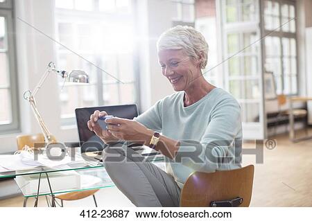 Stock Photo - Businesswoman using cell phone at home office desk. Fotosearch