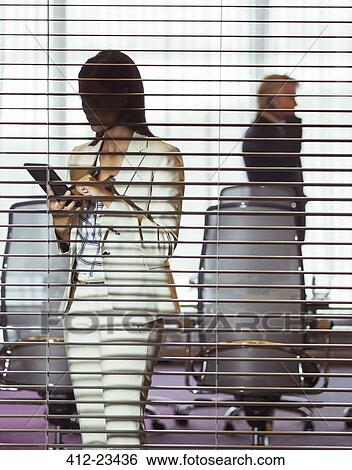 Stock Photograph - Businesswoman using tablet pc standing in conference room behind blinds. Fotosearch