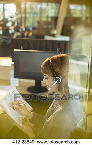 Stock Photo - Businesswoman wearing headset and working in office. Fotosearch
