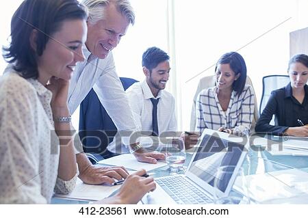 Businesswomen and businessmen sitting at conference table, using laptop and smiling View Large Photo Image Stock Image - Businesswomen and businessmen sitting at conference table, using laptop and smiling. Fotosearch