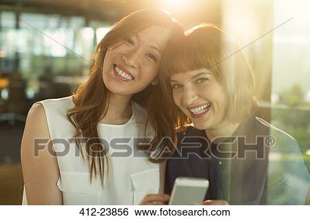 Businesswomen using cell phone in office View Large Photo Image Stock Photograph - Businesswomen using cell phone in office. Fotosearch