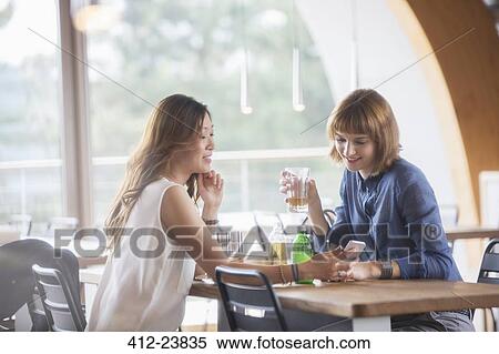 Businesswomen using cell phone in cafeteria View Large Photo Image Stock Photography - Businesswomen using cell phone in cafeteria. Fotosearch
