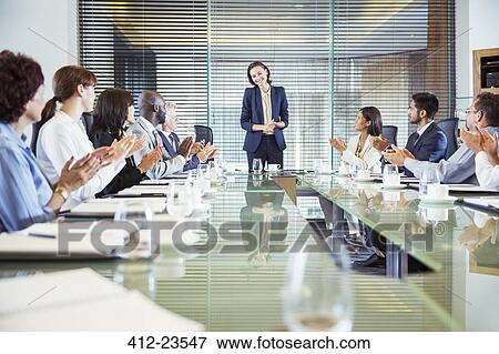 Stock Photo - Conference participants applauding to young businesswoman standing at head of conference table. Fotosearch