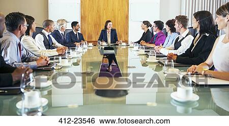 Conference participants looking at young woman sitting at head of conference table View Large Photo Image Stock Photograph - Conference participants looking at young woman sitting at head of conference table. Fotosearch