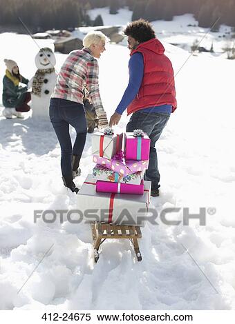 Stock Photography - Couple pulling sled with Christmas gifts in snow. Fotosearch