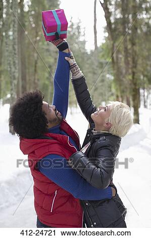 Couple reaching for Christmas gift in snow View Large Photo Image Stock Image - Couple reaching for Christmas gift in snow. Fotosearch