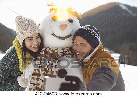 Stock Image - Couple taking selfie with snowman. Fotosearch