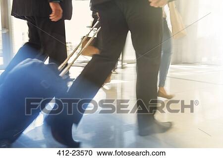 Stock Image - Cropped shot of two men walking side by side with trolley case. Fotosearch