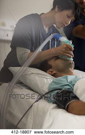 Doctor holding oxygen mask over male patient's mouth in intensive care unit View Large Photo Image Stock Photo - Doctor holding oxygen mask over male patient's mouth in intensive care unit. Fotosearch