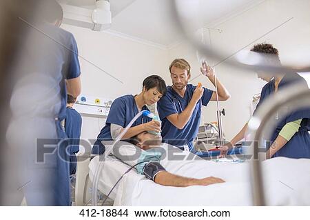 Picture - Doctor holding oxygen mask over patient, male doctor adjusting IV drip. Fotosearch