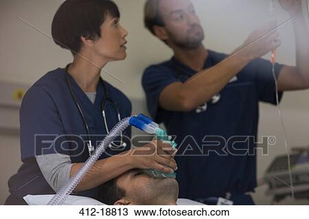 Doctor holding oxygen mask over patient, doctor adjusting IV drip in intensive care unit View Large Photo Image Stock Image - Doctor holding oxygen mask over patient, doctor adjusting IV drip in intensive care unit. Fotosearch